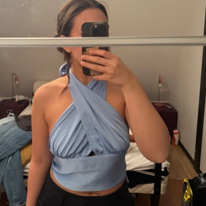 Ljusblå omlott topp - Snygg ljusblå omlott topp med knytning i ryggen. Toppen är ärmlös och har en öppen rygg vilket ger en stilren look. Perfekt för varma dagar eller en utekväll.