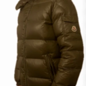 Olivgrön dunjacka från Moncler - Säljer en snygg olivgrön dunjacka från Moncler. Jackan har en quiltad design med dragkedja framtill och en praktisk huva. Perfekt för kyliga dagar med sin varma och stilrena look. 🧥