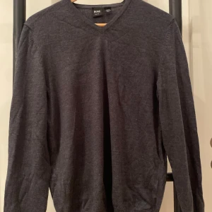 Mörkgrå tröja från Boss - Säljer en stilren mörkgrå tröja från Boss. Tröjan har en v-ringad design. Slim fit. 