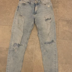 Ljusa jeans med slitningar från H&M - Snygga ljusblå jeans från H&M med coola slitningar på benen. Perfekta för en avslappnad stil. De har en klassisk femficksdesign och knappgylf.