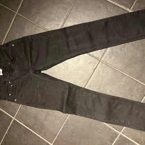 Svarta slimmy jeans från 157 - Snygga svarta slimmy jeans från 157. Perfekta för en stilren look med en smal passform. Klassisk design med fem fickor och knappgylf. Bredd 31, längd 32