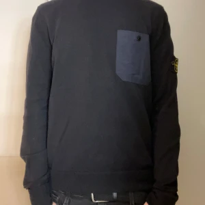 Svart långärmad tröja från Stone Island - Säljer en stilren svart långärmad tröja från Stone Island. Tröjan har en bröstficka med knapp och det ikoniska märket på ärmen. Perfekt för en casual look. Använd cirka 3 gånger som ny. Inga djur i hemmet. Jag är 179cm lång.