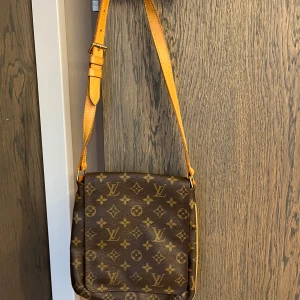 Brun axelväska från Louis Vuitton - Säljer en snygg brun axelväska från Louis Vuitton med det klassiska monogrammönstret. Väskan har en justerbar axelrem och är perfekt för att bära dina dagliga nödvändigheter. Tillverkad i Frankrike. Modellen heter Musette Salsa.