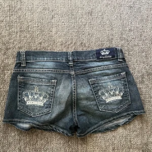 Jeansshorts victoria beckham - Snygga jeansshorts från Victoria Beckham med en cool broderad krona på bakfickorna. De har en klassisk femficksdesign och en knappgylf med dragkedja. Perfekta för en avslappnad stil med en touch av lyx. Storlek small. Ca 40 cm rakt över midjan.