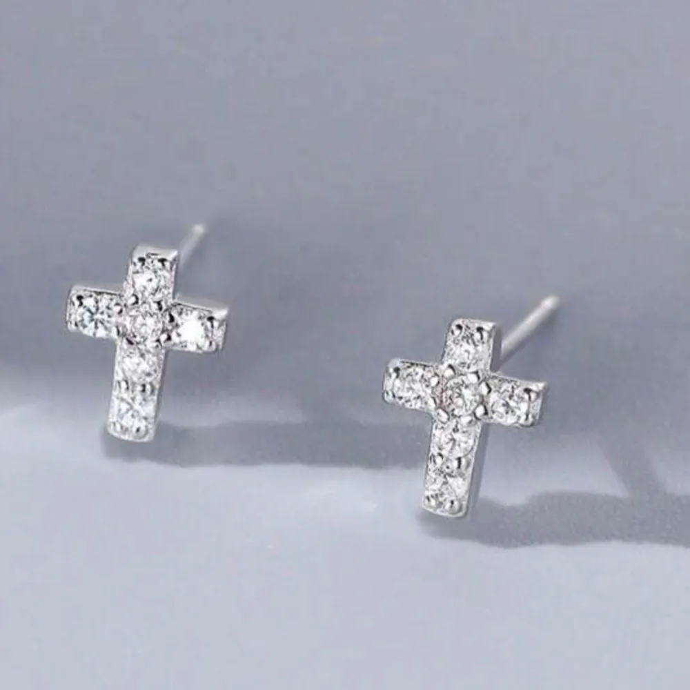 Eleganta små silvriga örhängen i form av kors, dekorerade med glittrande stenar. Perfekta för att ge en stilren touch till din look. Passar både till vardag och fest. 925 sterling silver (äkta silver). Asusteet.