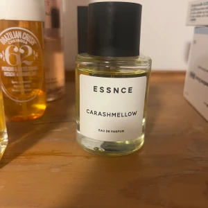 Essnce Carashmellow Eau de Parfum - Säljer en flaska Essnce Carashmellow Eau de Parfum. Flaskan är genomskinlig med en svart kork och har en enkel, stilren etikett. Doften är söt och krämig, perfekt för den som gillar mjuka och inbjudande parfymer.