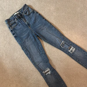 Blå skinny jeans med slitningar - Snygga blå skinny jeans med coola slitningar på knäna. Perfekta för en avslappnad stil. De har en klassisk femficksdesign och knappgylf.