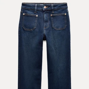 Mörkblå jeansbyxor - Snygga Flaer mörkblå jeansbyxor med klassisk femficksdesign och knappgylf. De har en rak passform och är perfekta för en avslappnad stil. Byxorna har en läderdetalj vid midjan baktill.