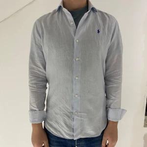 Ljusblå linneskjorta från Ralph Lauren - Ljusblå linneskjorta från Ralph Lauren med klassisk krage och knappar framtill. Storlek large. Modellen är 193cm lång och väger 85kg. 
