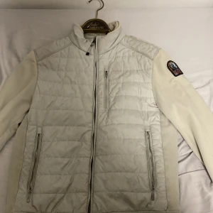 Beige/vit quiltad jacka från Parajumpers - Säljer en snygg vit/beige quiltad jacka från Parajumpers med dragkedja och broderad patch på ärmen. Jackan har långa ärmar och praktiska fickor med dragkedja. Perfekt för kyligare dagar!