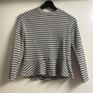 Grå och vit mönstrad tröja från Stockh LM - Snygg grå och vit mönstrad tröja från Stockh LM i storlek S. Tröjan har långa ärmar och ett unikt mönster som ger en stilren look. Perfekt för att addera lite mönster till din garderob.