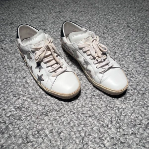  Saint Laurent skor - Snygga vita sneakers från Saint Laurent med coola stjärndetaljer i silver på sidorna. Skorna har snörning och en kontrasterande svart häl. Perfekta för en stilren look. Endast skor ingår. Fint skick