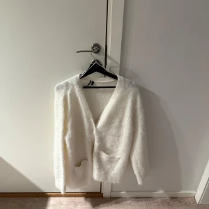 Vit fluffig kofta - Mysig vit kofta med en fluffig textur från bikbok. Den har långa ärmar och två fickor framtill. Perfekt för kyliga dagar när du vill ha något bekvämt och stilrent. Koftan är i storlek M och nypris är 600, mitt pris 350💕