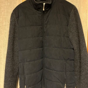 Marinblå jacka från Gran Sasso - Snygg jacka från Gran Sasso med quiltad svart framsida och blå stickade ärmar. Jackan har dragkedja framtill och är en vår och höstjacka. Den har en stilren design med ribbade detaljer och är långärmad.