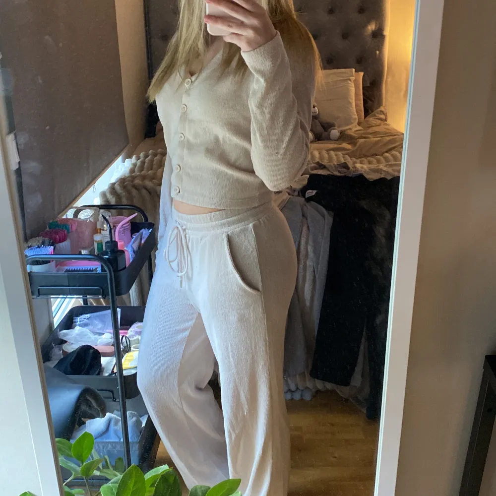 Säljer en beige ribbat set med knappar framtill. Den har en croppad design och långa ärmar, perfekt för en avslappnad stil. Koftan är mjuk och bekväm, idealisk för mysiga dagar hemma och byxorna är slappa men ändå sååå snygga . Neuletakit & Villapaidat.