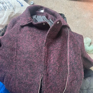 Vinröd ulljacka från H&M - Säljer en snygg vinröd ulljacka från H&M med dragkedja framtill. Jackan har en klassisk krage och är perfekt för kyligare dagar. Den är fodrad för extra värme och komfort.