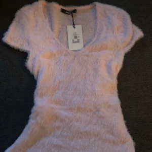 Ljusrosa fluffig klänning från Bik Bok - Säljer en supermjuk och fluffig ljusrosa topp från Bik Bok. Den har en v-ringad design och korta ärmar, perfekt för en mysig look. Toppen är i en tight passform och ger en unik stil. aldrig använt!❤️ nypris 299kr