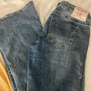 Blå jeans från True Religion - Snygga blå jeans från True Religion med klassisk femficksdesign och märkets ikoniska logga på bakfickan. Jeansen har en knappgylf och är tillverkade i slitstarkt denim. Perfekta för en avslappnad stil.