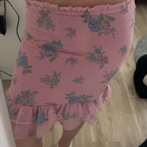 Rosa blommig kjol med volang - Säljer en söt rosa kjol med blommigt mönster💗 Kjolen är tight och har en volangdetalj längst ner💗 hör av er om ni önskar fler bilder på kjolen!  