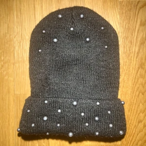 Svart stickad mössa med pärlor - Snygg svart stickad mössa dekorerad med små pärlor. Perfekt för att ge din vinterlook en extra touch. Den har en uppvikt kant och är både stilren och trendig.🤍