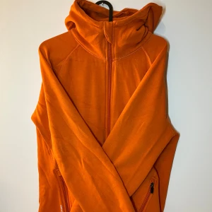 Orange fleecejacka med huva - Säljer en snygg orange fleecejacka med huva och dragkedja framtill. Tröjan har långa ärmar och fickor med dragkedja. 