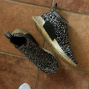 Adidas NMD sneakers i svartvitt mönster - Snygga Adidas NMD sneakers med ett unikt svartvitt mönster. Skorna har en elastisk ovandel för enkel påtagning och en bekväm sula. Perfekta för en stilren och modern look. Strl 40