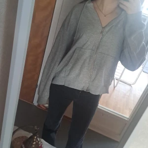 Grå hoodie med dragkedja - Säljer en bekväm grå hoodie med dragkedja och fickor framtill. Perfekt för en avslappnad stil. Den har långa ärmar och en luva för extra mysfaktor.