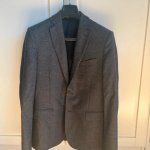 Grå kavaj från J.Lindeberg - Snygg grå kavaj från J.Lindeberg i klassisk design. Perfekt för både formella och semi-formella tillfällen. Kavajen har en stilren passform med två knappar framtill och en bröstficka. Pris kan diskuteras.