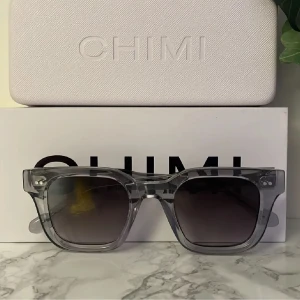 Transparenta solglasögon från Chimi - Snygga transparenta solglasögon från Chimi med en fyrkantig form. De har mörka linser som ger en cool kontrast till den klara bågen. Perfekta för att ge en stilren touch till din look.