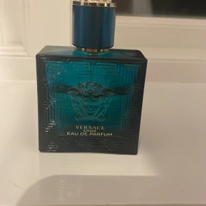 Versace Eros Eau de Parfum - Säljer en elegant Versace Eros Eau de Parfum i en stilren blå flaska med guldiga detaljer. Flaskan har en fyrkantig form och pryds av det ikoniska Medusa-huvudet. Perfekt för den som vill ha en doft med karaktär och stil.35 ml