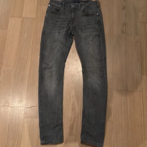 Grå jeans från Scotch & Soda - Snygga grå jeans från Scotch & Soda med en klassisk femficksdesign. De har en straight passform och är tillverkade i ett slitstarkt denimtyg. Perfekta för en stilren look.
