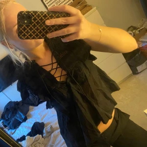 Neo noir svart blus med volangdetaljer  - Snygg svart blus med volangdetaljer och knytning framtill. Perfekt för både vardag och fest!😍 Den har korta ärmar och en luftig passform som gör den bekväm att bära. Köpt i butik på Nelly med prislapp kvar så aldrig använd! Köpt för 600kr💕💕💕