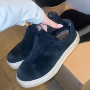 Svarta Eytys - Säljer ett par svarta sneakers i mocka med vit sula. Skorna har en stilren design utan snörning, vilket ger dem ett minimalistiskt utseende. Perfekta för en avslappnad stil.