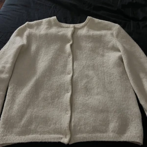 Vit kofta från H&M - Säljer en stilren beige kofta från H&M i storlek XS. Koftan har långa ärmar och knäppning framtill med små vita knappar. Köpt för 200kr