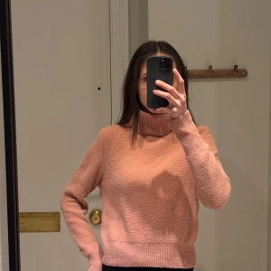 Rosa stickad polotröja - Mysig rosa stickad polotröja med långa ärmar. Tröjan har en hög polokrage och ribbade muddar vid ärmslut och nederkant.