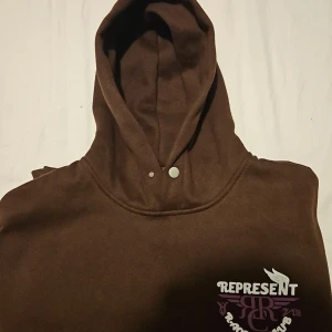 Brun four cactus hoodie  - Säljer en brun hoodie från four cactus med trycket 'Represent Racing Club' i vitt och lila på bröstet och ryggen. Hoodien har en klassisk känguruficka och en bekväm passform. Perfekt för en avslappnad stil. Aldrig använd fick i julklapp av farmor. 