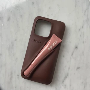 Espresso mobilskal från Rhode, IPhone 14 Pro (läppstift på köpet) - Brunt (espresso) mobilskal från Rhode med en unik design. Skalet har en slät yta med subtila linjer som ger ett modernt utseende. Perfekt för att skydda din telefon med stil. Passar iphone 14 pro. Ni får med läppstift färgen toast på köpet :)