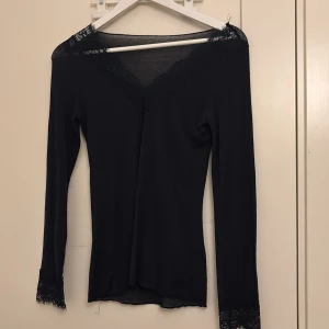 Mörkblå långärmad topp med spetsdetaljer - Elegant svart mörkblå topp med spetsdetaljer vid halsringning och ärmslut. Perfekt för en stilren look.
