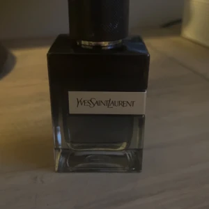 Parfym från Yves Saint Laurent - Elegant parfymflaska från Yves Saint Laurent med en stilren design. Flaskan är fyrkantig med en mörk tonad glasfinish och svart lock. Perfekt för den som söker en sofistikerad doftupplevelse. Då jag fått en ny parfym jag använder mig av så står ysl bara och dammar. 20ml utav 60ml använd. Nypris 1150