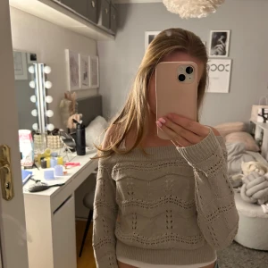 Beige stickad offshoulder-tröja - Säljer en snygg beige stickad offshoulder-tröja med ett fint hålmönster. Tröjan har långa ärmar och en bekväm passform. Perfekt för en stilren och avslappnad look.