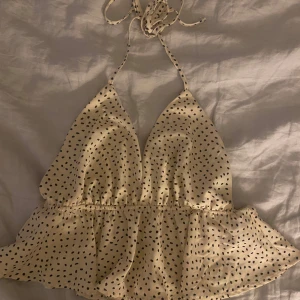 Prickig ärmlös topp - Säljer en söt prickig topp med volangdetaljer och knytning i nacken. Toppen är ärmlös och har en luftig passform, perfekt för varma dagar💕