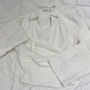 Blus från NA-KD - Snygg vit omlottblus från NA-KD med knappar och långa ärmar. Perfekt för en stilren look. Can be tighted on the side- arms are tight on bicep and big on wrist to create a stylish style. 