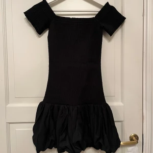 Svart klänning från H&M - Snygg svart klänning från H&M med en tight passform och korta ärmar. Klänningen har en volangdetalj vid fållen som ger en extra touch. Perfekt för en stilren look.