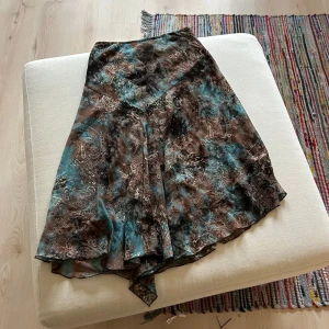 Mönstrad kjol i blå och brun - Säljer en fin Lågmidjad midi/maxi kjol med ett paisleymönster i blå och brun. Kjolen har en asymmetrisk form och är tillverkad i ett lätt och flödande material. Både lite fairycore och bohemisk 🥹 väldigt bra skick!! 