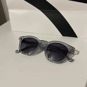 Grå transparenta solglasögon från Sayless - Snygga grå transparenta solglasögon från Sayless med rundad form. De har mörka linser och en stilren design som passar perfekt för soliga dagar. Logotypen är subtilt ingraverad på skalmen.