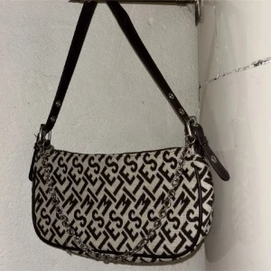 Mönstrad axelväska med kedjedetalj - Snygg axelväska med ett unikt mönster i svart och beige. Väskan har en kedjedetalj och justerbar axelrem i mörkt skinn. Perfekt för att ge din outfit en trendig touch.