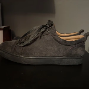 Gråa sneakers från Christian Louboutin 42 - Snygga grå sneakers i mocka från Christian Louboutin med den ikoniska röda sulan. Skorna har snörning och en stilren design.