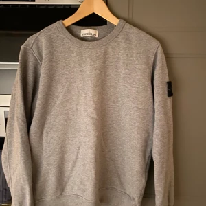 Grå sweatshirt från Stone Island - Säljer en stilren grå sweatshirt från Stone Island med deras märke på ärmen. Köpt på NK för 2999 för ungefär två år sedan man använts fåtal gånger. 9/10 skick, äkthet garanteras! Finns ej kvitto men qr kod som skannar