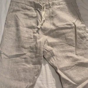 Beige linnebyxor från NN07 - Snygga beige byxor från NN07 i linne med avslappnad passform. De har praktiska fickor och en bekväm snörning i midjan. Perfekta för varma sommardagar! Pris kan diskuteras