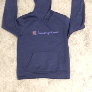 Blå hoodie från Champion - Säljer en snygg blå hoodie från Champion med deras ikoniska logga på bröstet. Tröjan har en praktisk magficka och en bekväm huva. Perfekt för en avslappnad stil.